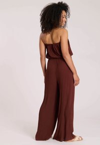 Jumpsuit marrone senza spalline con una vestibilità rilassata, tessuto testurizzato, gambe larghe e vita cintrata, dotato di un top elasticizzato per il comfort.