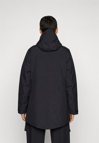 Czarna wodoodporna kurtka z kapturem, o luźnym kroju, elastycznych mankietach i dłuższym tylnym rzędzie dla dodatkowej ochrony. Minimalistyczny design.