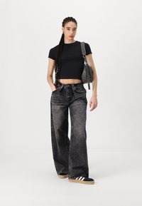 T-shirt noir court associé à un jean foncé taille haute à jambes larges. Les accessoires incluent un sac à main gris et des baskets noires avec des rayures blanches.