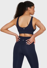 Sportivo color navy con spalline larghe e logo sulla schiena; abbinato a leggings navy a vita alta con una texture liscia e cuciture minime.