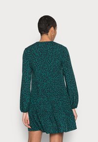 Grönmönstrad klänning med långa ärmar, har en rund halsringning och en utsvängd nederkant. Tyget har en blommönstring i mörkare nyanser.