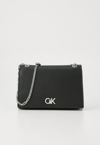 Sac en cuir noir avec un design pliable, une chaîne argentée et un logo argenté prominent sur le devant. Texture lisse, style minimaliste.