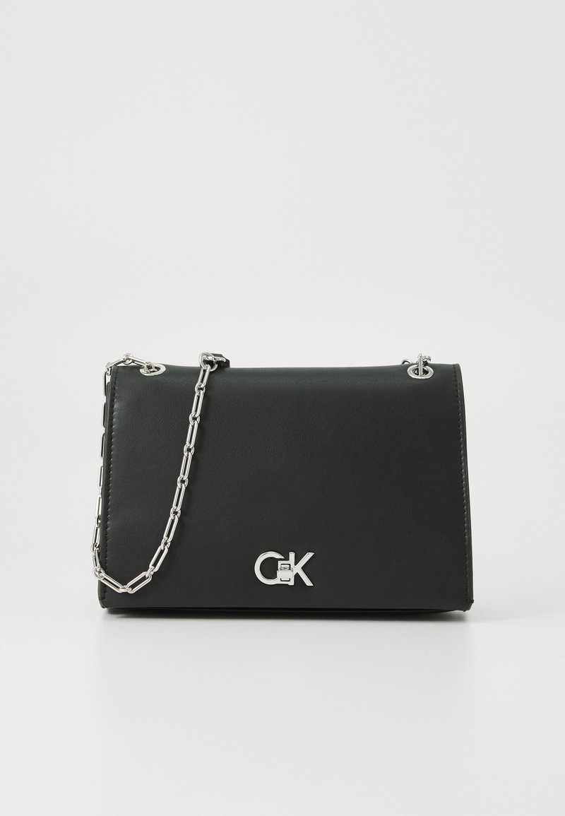 Sac en cuir noir avec un design pliable, une chaîne argentée et un logo argenté prominent sur le devant. Texture lisse, style minimaliste.