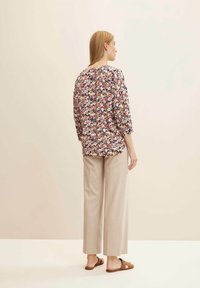 Blouse florale avec une coupe décontractée, dotée de manches 3/4 et d'un col rond, associée à un pantalon large beige clair et des sandales marron.