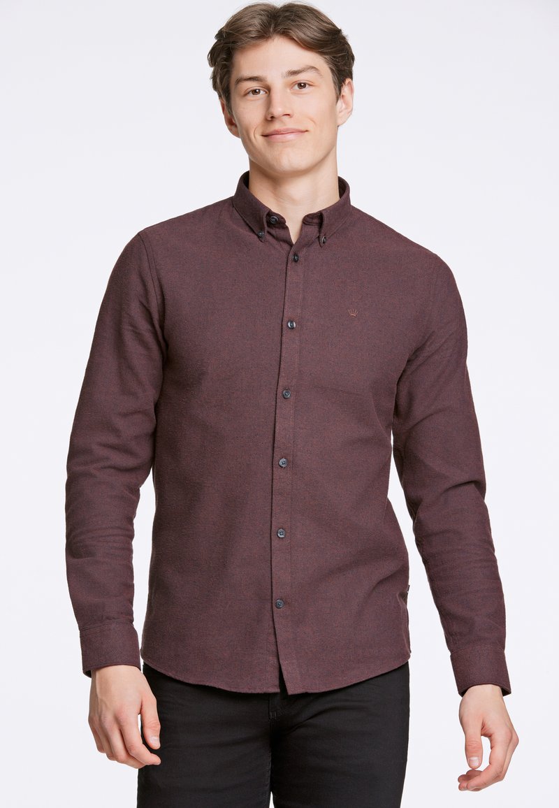 Camicia button-up bordeaux con finitura texturizzata, bottoni neri e un piccolo logo sul petto, abbinata a pantaloni neri.