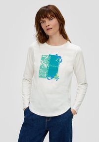Chemise blanche à manches longues avec un design graphique coloré, incluant des rectangles bleus et verts ainsi que du texte. Tissu doux avec une coupe décontractée.