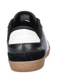 Zwart-witte sneaker met een gestructureerde leren bovenkant, stofaccenten en een lichtbruine rubberen zool met een subtiele glinsterende afwerking.