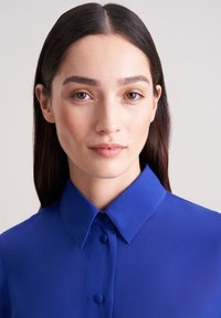Blau geknöpfte Bluse mit glatter Textur, die über eine klassische Gestaltung verfügt und eine satte blaue Farbe hervorhebt.