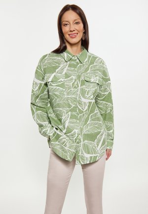 Groene overhemd met knopen, gekenmerkt door een wit bladerenpatroon, grote kraag en twee borstzakken, gecombineerd met lichtbeige broeken.