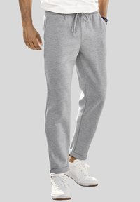 Graue Sweatpants aus weichem Stoff, mit einem Kordelzugbund, schmal zulaufenden Beinen und seitlichen Taschen, kombiniert mit weißen Sportschuhen.