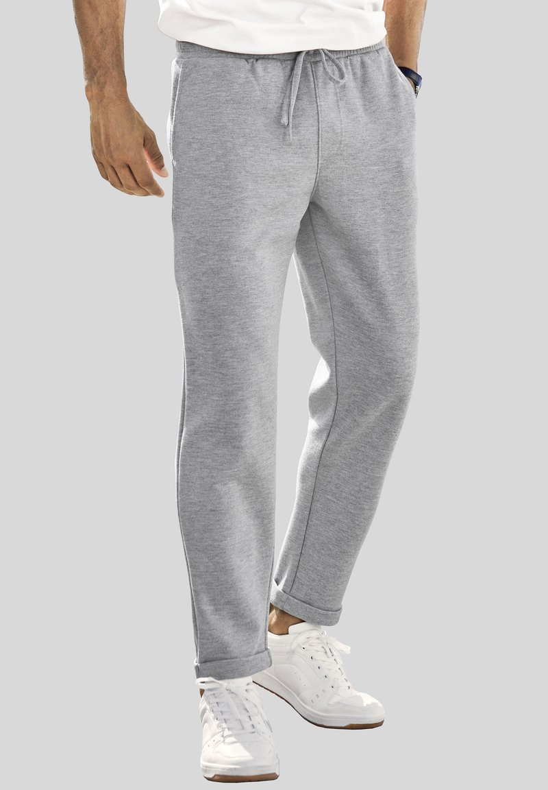 Graue Sweatpants aus weichem Stoff, mit einem Kordelzugbund, schmal zulaufenden Beinen und seitlichen Taschen, kombiniert mit weißen Sportschuhen.