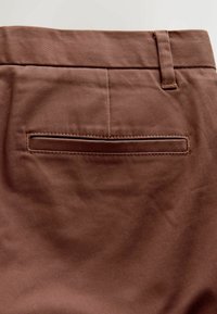 Braune Baumwollhosen mit glatter Textur, ausgestattet mit einer einzelnen Gesäßtasche und Gürtelschlaufen an der Taille. Die Nähte ergänzen das Design.