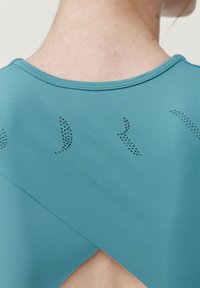 Teal urheilu paita pyöreällä kaula-aukolla, jossa on leikkaus yksityiskohta selässä ja koristeellinen pistekuvio yläselässä.