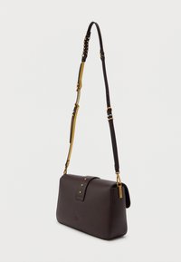 Σκούρο καφέ δερμάτινη τσάντα ώμου με ρυθμιζόμενο λουρί, χρυσές καρφίτσες και μια μικρή ανάγλυφη λεπτομέρεια πεταλούδας στο μπροστινό μέρος, σε απλό φόντο.