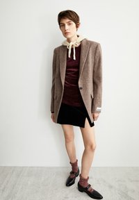 Blazer en laine marron sur un top en velours bordeaux, associé à une mini-jupe en velours noir et des chaussures noires avec des chaussettes chevilles. Design simple et texturé.