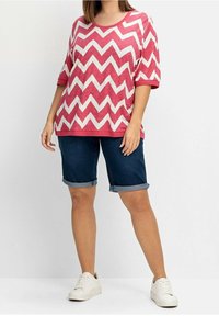 Růžový a bílý top se vzorem cikcak, krátké rukávy, kombinovaný s tmavými džínovými šortkami s ohrnutým lemem a bílými teniskami. Ležérní střih a strukturovaná látka.