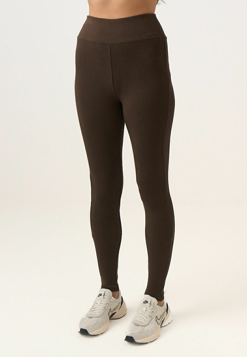 Barna bordázott leggings, magas derékkal és sima textúrával; logó a derékpánton; világosszürke sportcipővel párosítva.