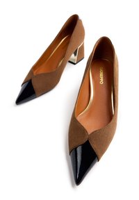 Tacones altos de ante marrón con puntera de charol negro y tacón metálico. El interior presenta acentos dorados y un acabado suave.