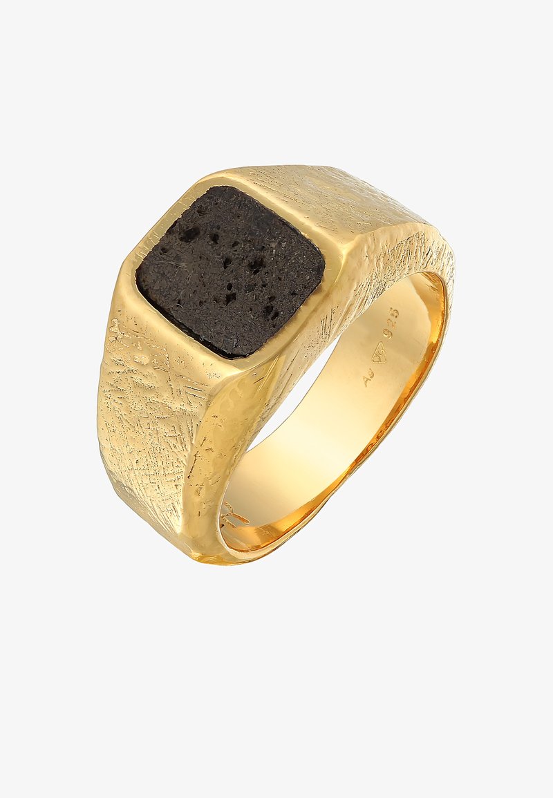 Bague en métal doré avec un anneau texturé, comportant un sertissage carré en pierre noire sur le dessus. La surface a une finition brossée et des détails complexes.