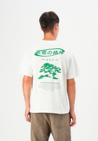 White cotton t-shirt featuring a green graphic print on the back with Japanese text, depicting a tree and phrases about care and patience.