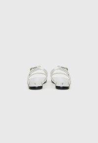Silver sandals with wide straps and textured accents, flat black rubber soles, and a minimalist design. Adjustable buckle detail at the side.