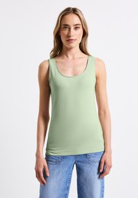 Top senza maniche verde chiaro con scollatura rotonda e spalline larghe, realizzato in un tessuto morbido ed elasticizzato. Abbinato a jeans in denim blu.