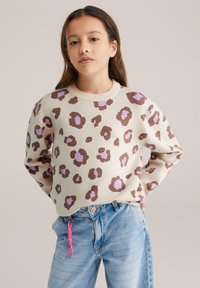 Pull beige clair avec un imprimé léopard en marron et lavande, col rond, manches longues et coupe décontractée. Associé à un jean en denim bleu.