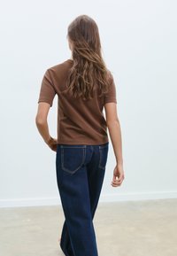 Brun topp med korta ärmar i mjukt tyg, kombinerad med mörkblå jeans med hög midja, kontrastsömmar och bakfickor.