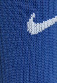 Sinine kudumine, millel on ribiline tekstuur, keskel valge Nike swoosh logo, detailne õmblus on nähtav.