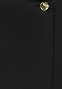 Gros plan sur un tissu noir avec des coutures visibles et un seul bouton doré brillant près d'une boutonnière.