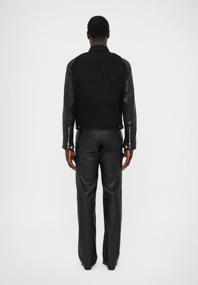 Jachetă neagră cu mâneci din piele, fermoare pe manșete și un design ajustat. Asortată cu pantaloni negri din piele, scoțând în evidență o siluetă elegantă.