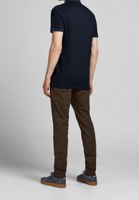 Marinblå polo-Shirt med korta ärmar, bruna byxor och grå sneakers med gummisulor. Slimmad stil, avslappnad design och slät textur.