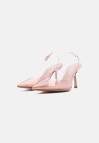 Ζευγάρι διαφανών ροζ γοβών με ψηλά τακούνια, λουράκια που στηρίζονται στον αστράγαλο και μυτερές μύτες, σε λευκό φόντο.