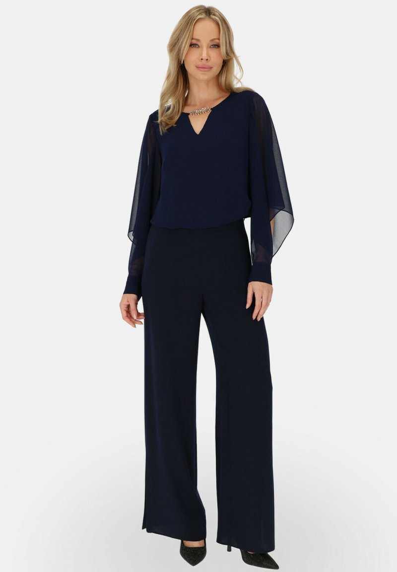Granatowy zestaw składający się z warstwowej bluzki z przezroczystymi rękawami, wykończonej dekoltem w kształcie V i ozdobami, dopasowany do szerokich spodni i spiczastych szpilek.