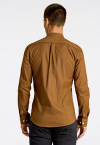 Camisa marrón de manga larga con botones, corte recto, detalle de pliegue en la parte posterior y puños con botones; tela suave con una textura sutil.