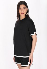 Sort kortærmet top med hvide detaljer ved ærmekanterne, parret med sorte shorts med hvide kanter. Glat tekstur, afslappet pasform.
