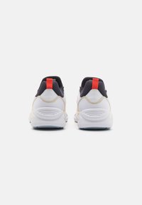 Paire de baskets blanches avec doublure intérieure noire et languettes de tirage rouges, vues de dos sur un fond blanc.