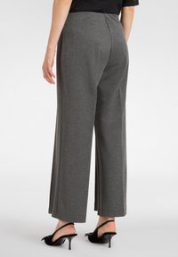 Szare szerokie spodnie o gładkiej teksturze, z średnim stanem i tylniymi kieszeniami. Noszone z czarnymi szpilkami na pasku.