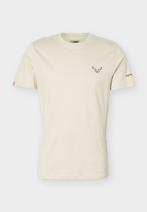 Beige kurzärmliges T-Shirt mit Rundhalsausschnitt, schwarzem Tiergesichtslogo auf der Brust und kleinem Text am linken Ärmel.