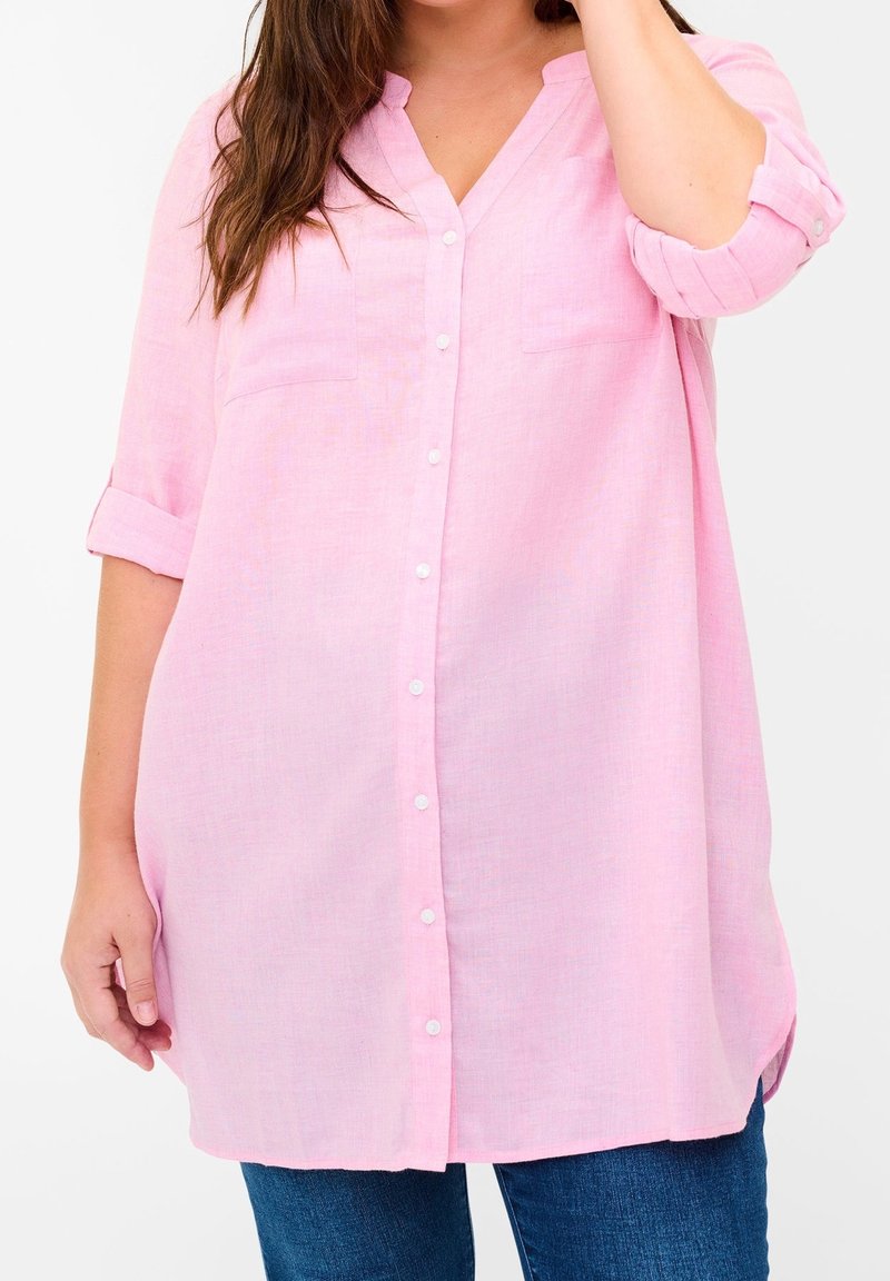 Camicia button-up rosa chiaro in un tessuto leggero, caratterizzata da un colletto a V, maniche arrotolabili e due tasche sul petto. L'orlo è curvato ai lati.