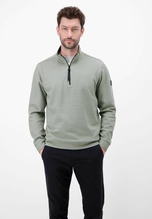 Jasnozielony pulower z zamkiem błyskawicznym przy szyi, z teksturowanym wzorem, ściągaczami na mankietach oraz czarnym zamkiem. Noszony z ciemnymi spodniami. Minimalistyczny design.