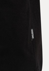 Svart bomull t-shirt med en mjuk textur, med en liten, vit märkeslapp på sidan. Enkla designen, korta ärmar och rundad halsringning.