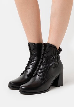 Bottines noires en cuir avec un embout arrondi, des lacets et un détail froncé au niveau de la cheville. Elles disposent d'un large talon bloc.