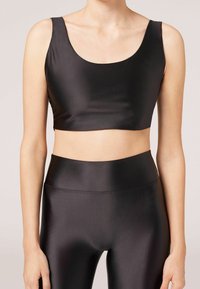 Svart atletisk kort topp med en slät, glänsande tyg, breda axelremmar och rundad halsringning, i kombination med matchande högmidjade leggings.
