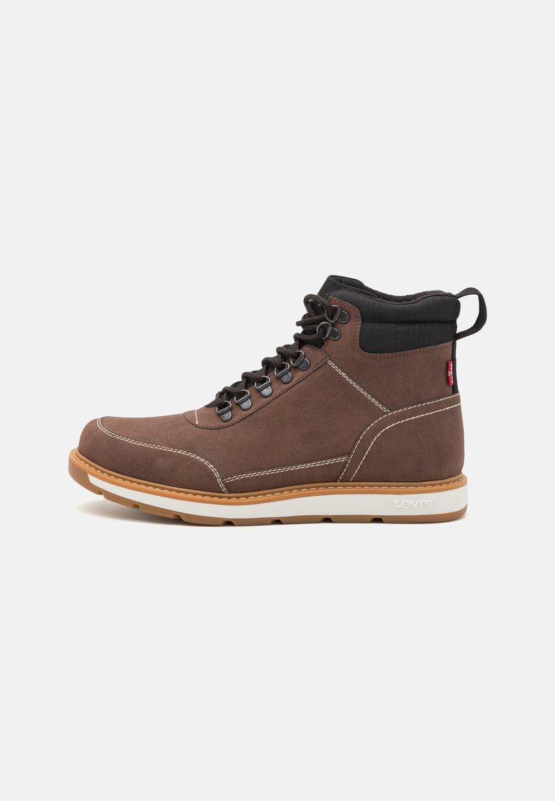 Bota de ante marrón de media caña con suela blanca, cuello negro, costuras en contraste y ojales de metal para los cordones. Diseño duradero con una lengüeta.