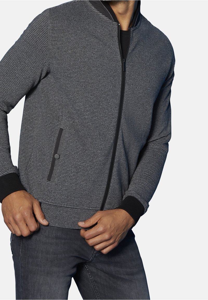 Grijze zip-up jas van textuur met ribbels aan de manchetten en kraag, voorzien van twee zijzakken met zwarte accenten. Geschikt voor casual wear.