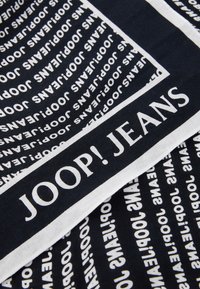 Black fabric featuring repeated white text "JOOP! JEANS" in varying orientations, with a white border along the bottom edge.