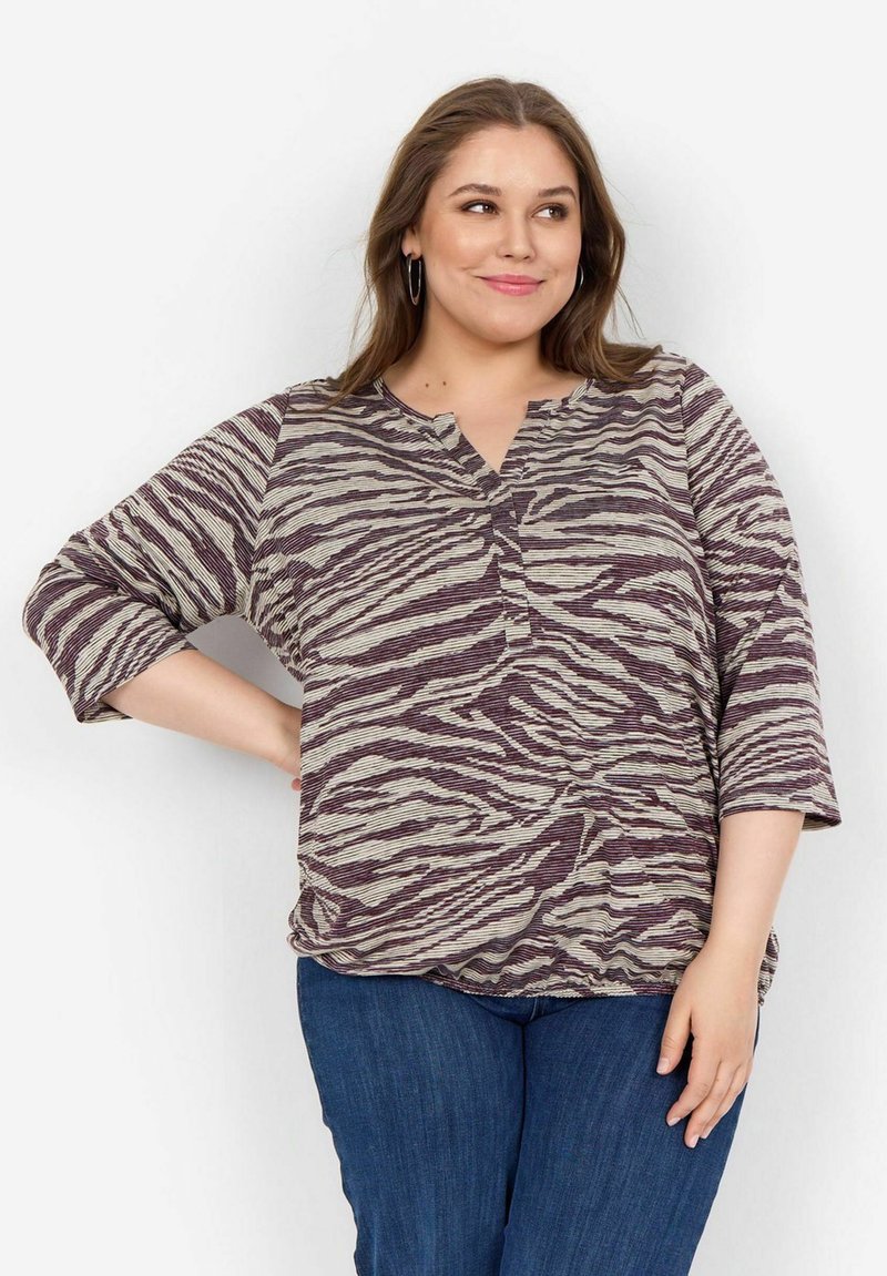 Top a righe viola e crema, con vestibilità morbida, scollatura a V e maniche di tre quarti. Tessuto morbido e strutturato. Abbinato a jeans blu.