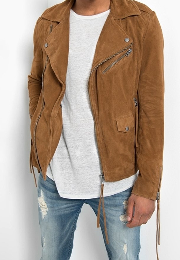 Veste de moto en daim marron avec détails zippés, revers crantés et poches, associée à un t-shirt gris clair et un jean bleu déchiré.