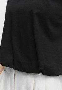 Czarna bawełniana bluzka o luźnym, swobodnym kroju, z gładką teksturą i miękkim opadaniem. Noszona na jasnych, wysokich spodniach.